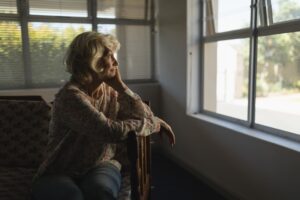 Starsza Pani patrząca przez okno, które być może cierpi na zaburzenia psychiczne w okresie starości